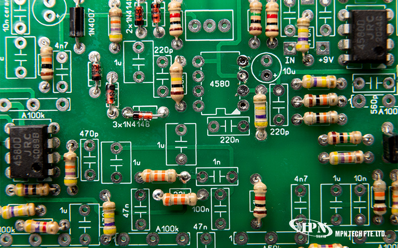 Close-up of green printed circuit board with labeled resistors, capacitors, diodes, and integrated circuits.