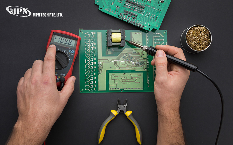 A technician using a soldering iron and multimeter to work on a printed circuit board (PCB).
