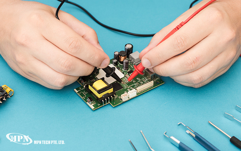 A close-up of a technician's hands using red and black probes to test a printed circuit board