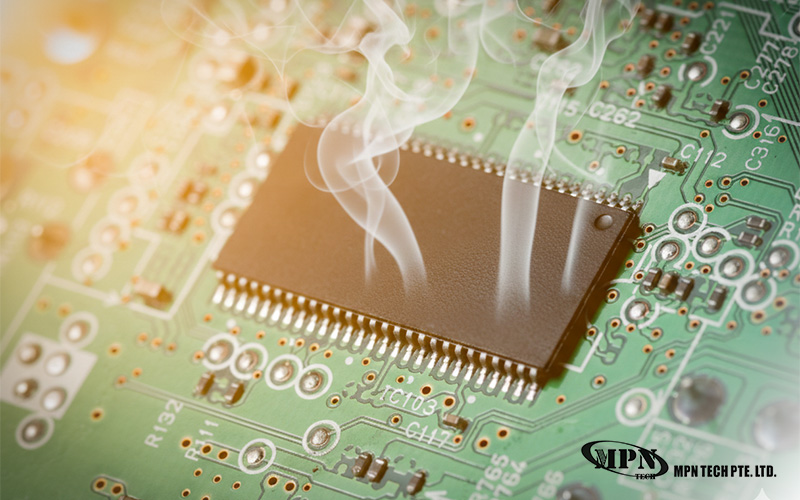 Smoke rising from a black integrated circuit chip on a green circuit board.
