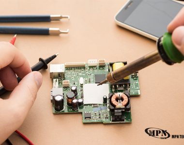 A person uses a soldering iron and multimeter probe on a green circuit board.