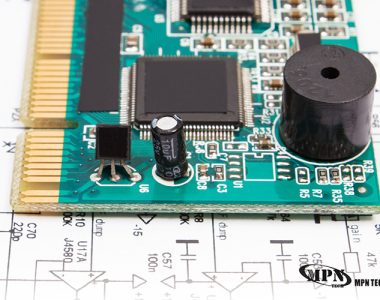 A green printed circuit board (PCB) sits on top of a white technical schematic diagram, showing various mounted electronic components like capacitors and microchips.