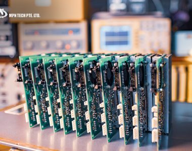 A row of green printed circuit boards (PCBs) lined up for inspection in a manufacturing facility.
