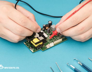 A close-up of a technician's hands using red and black probes to test a printed circuit board